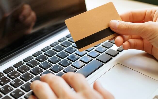 foto de uma pessoa fazendo compra na internet com um cartão e verificando uma devolução de compra pela internet como fazer
